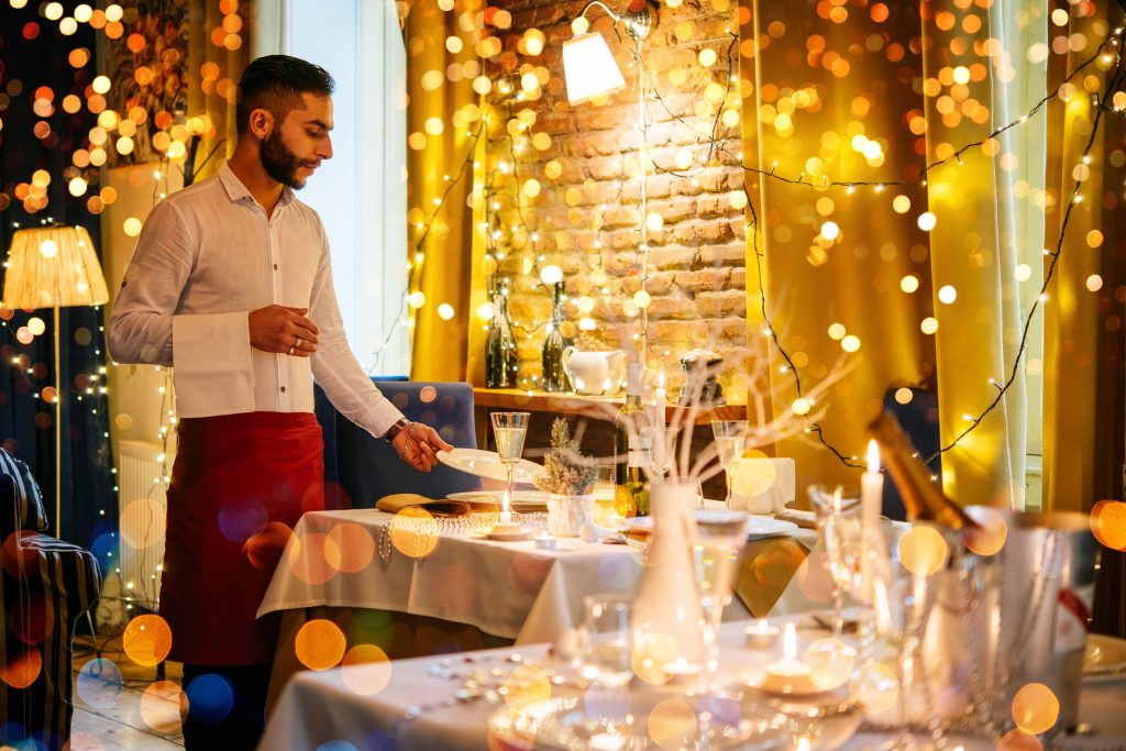 A waiter sets a table in a venue with lots of fairy lights