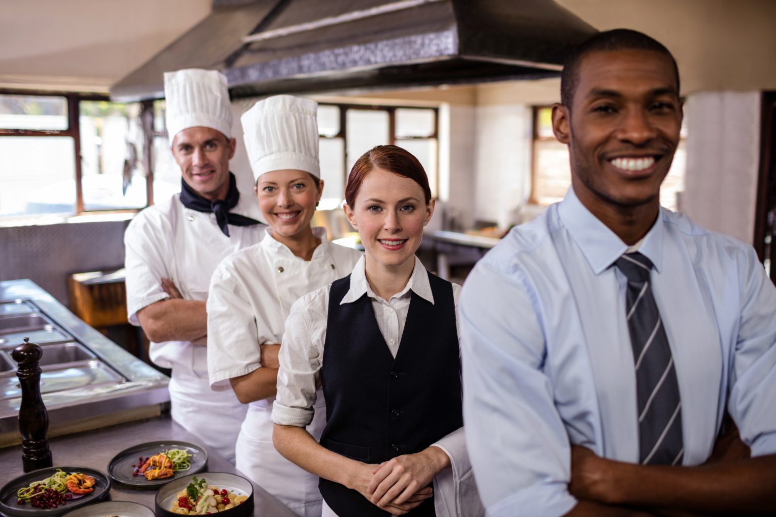 Group of hospitality staff standing with arms crossed in kitchen