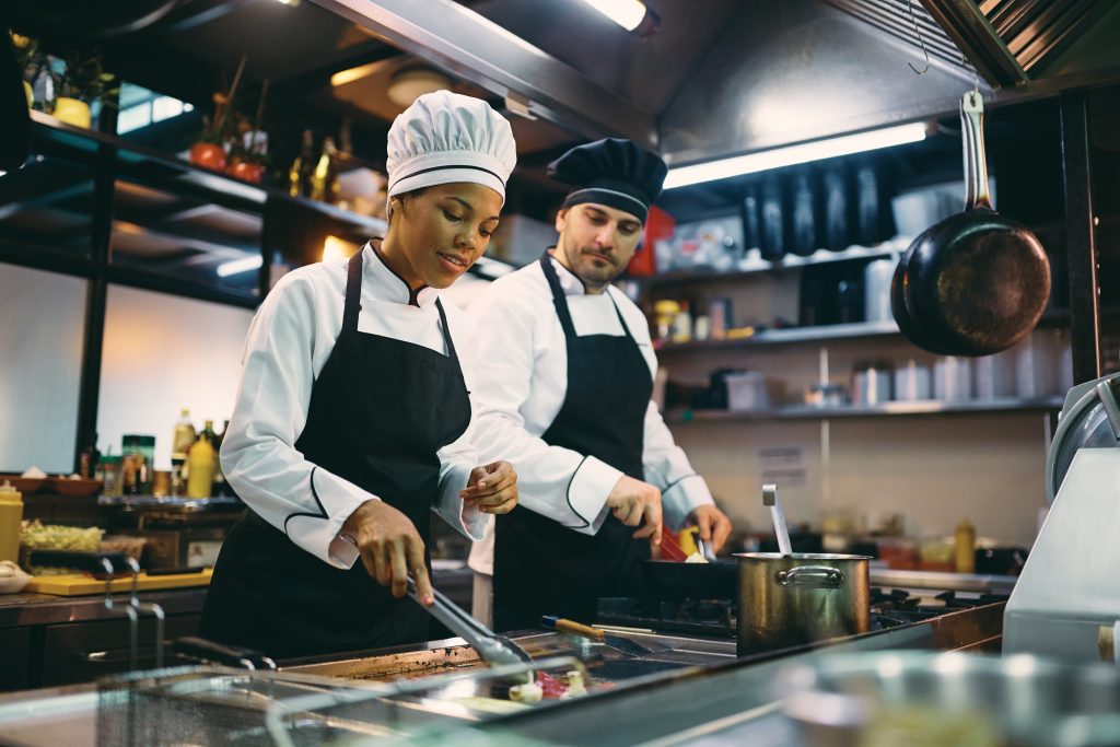Two professional cooks preparing meal in the kitchen at restaurant.